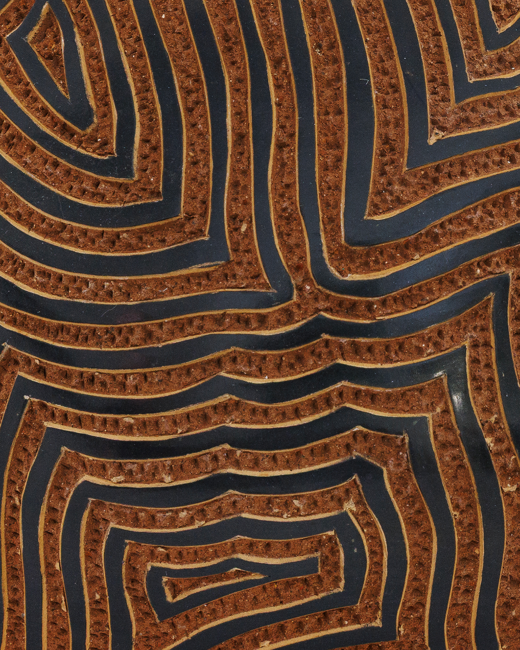 Amaru: handmade Nicaraguan ceramic rounded terracotta vessel carved with concentric maze-like lines and a black glazed neck, close-up of the carved texture