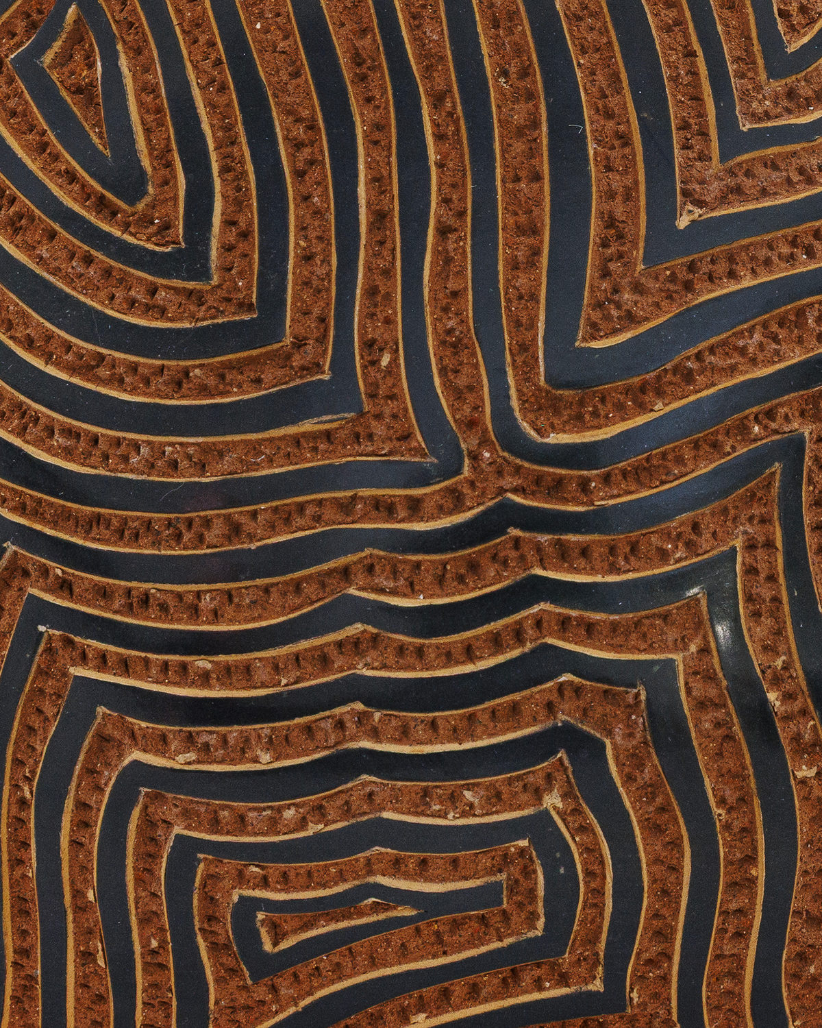 Amaru: handmade Nicaraguan ceramic rounded terracotta vessel carved with concentric maze-like lines and a black glazed neck, close-up of the carved texture