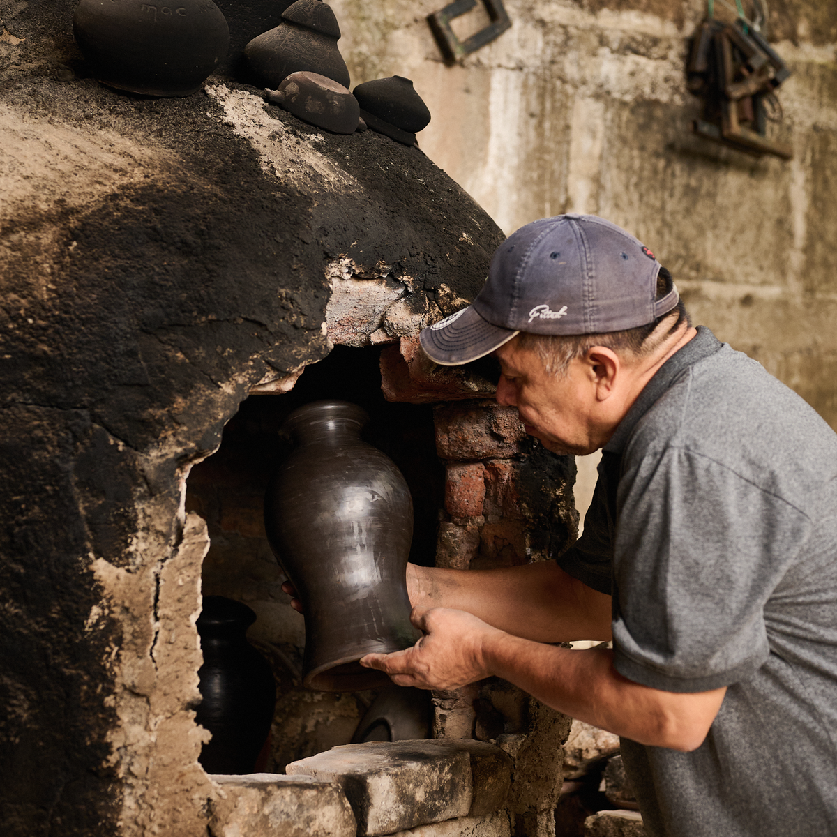 An artisan placing a clay vessel into a traditional kiln