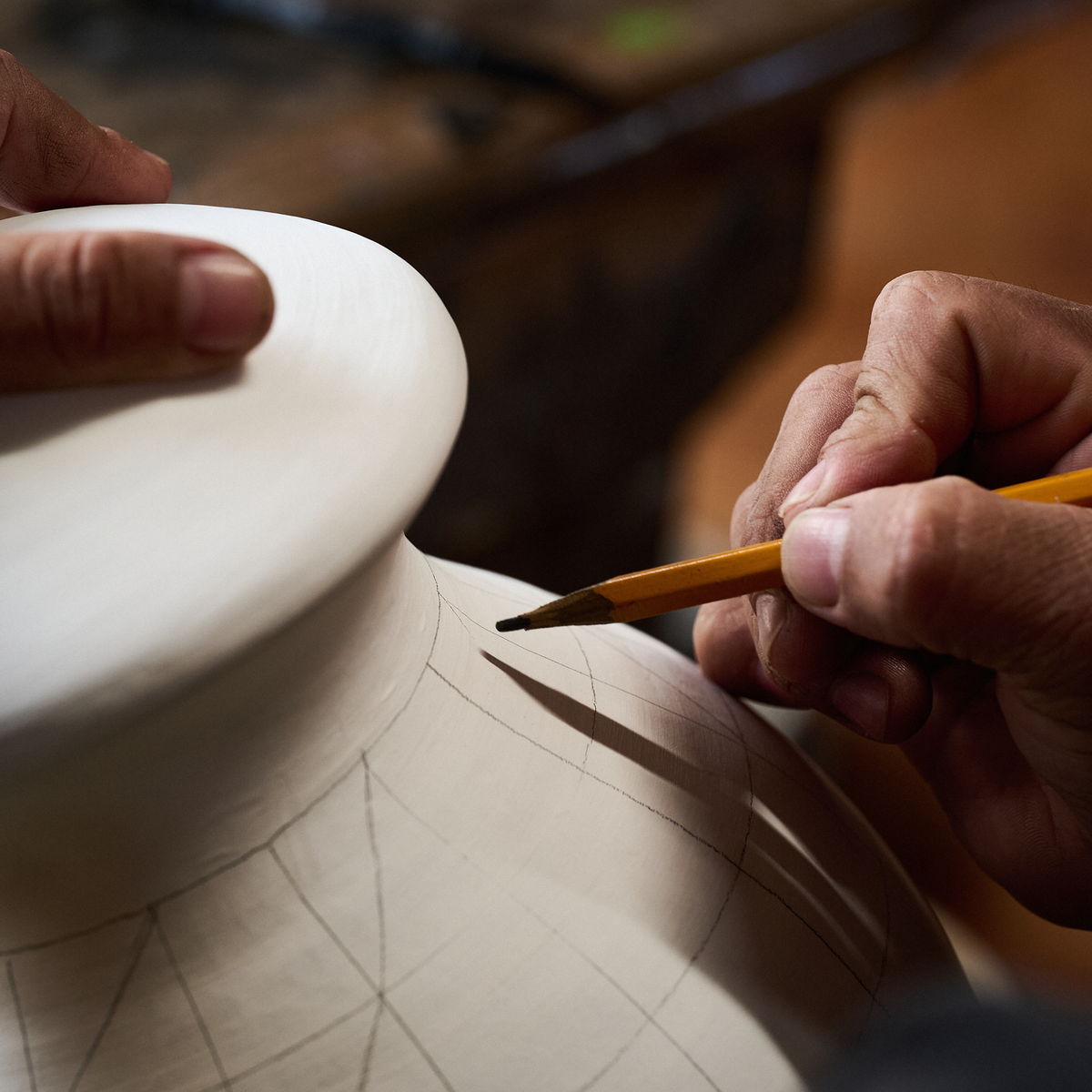 An artisan drawing a pattern in pencil onto an unfired clay vessel