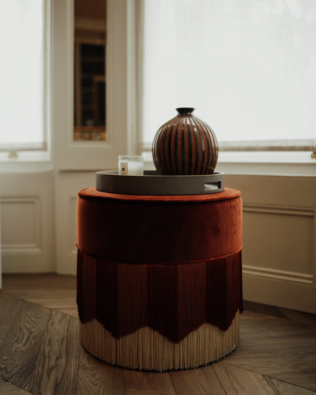 Amapola: handmade Nicaraguan ceramic round vessel with glossy black and textured terracotta vertical stripes, on a fringed velvet stool in a sunlit room