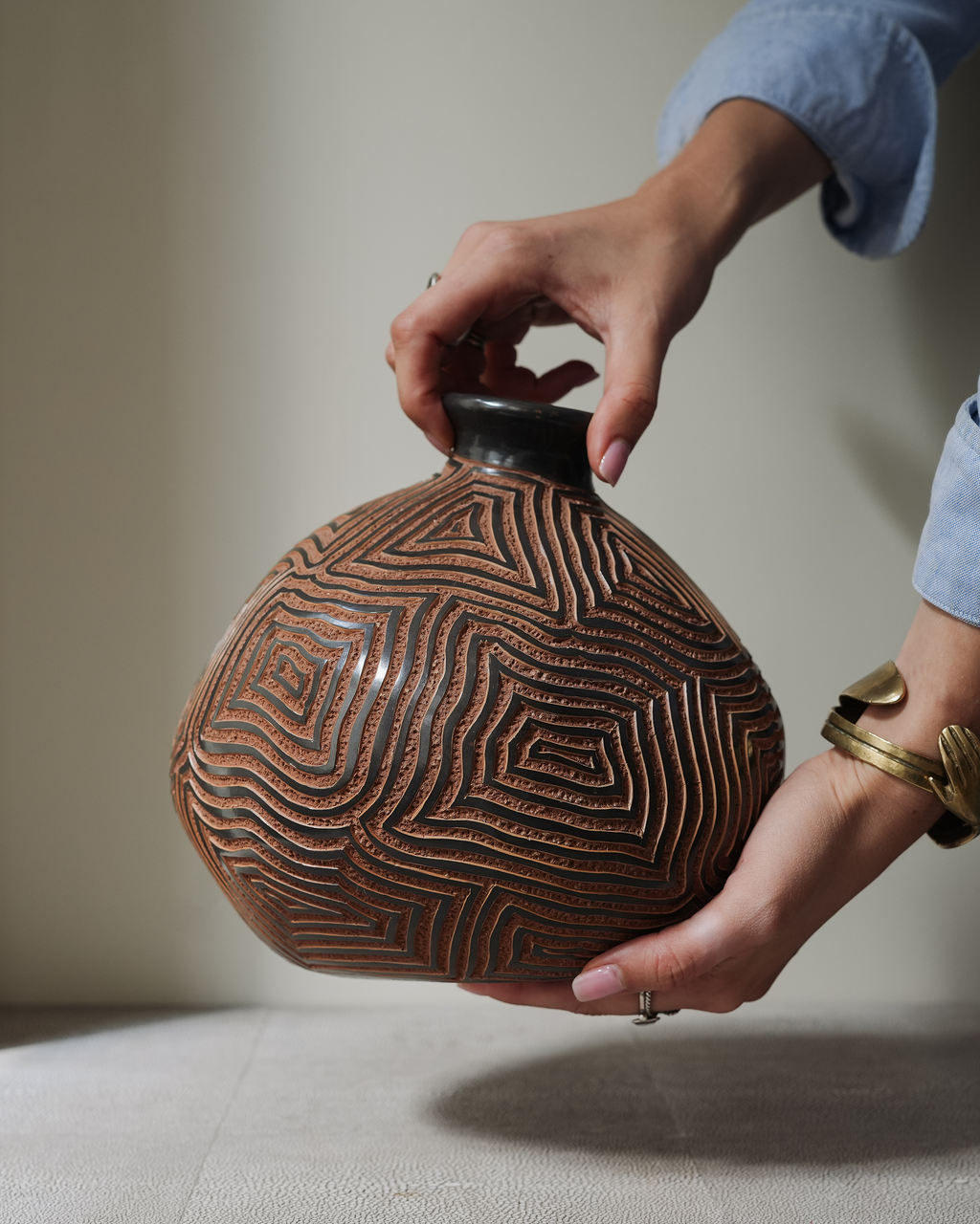 Etrana: handmade Nicaraguan ceramic brown vessel carved with a concentric maze pattern, lifted in two hands