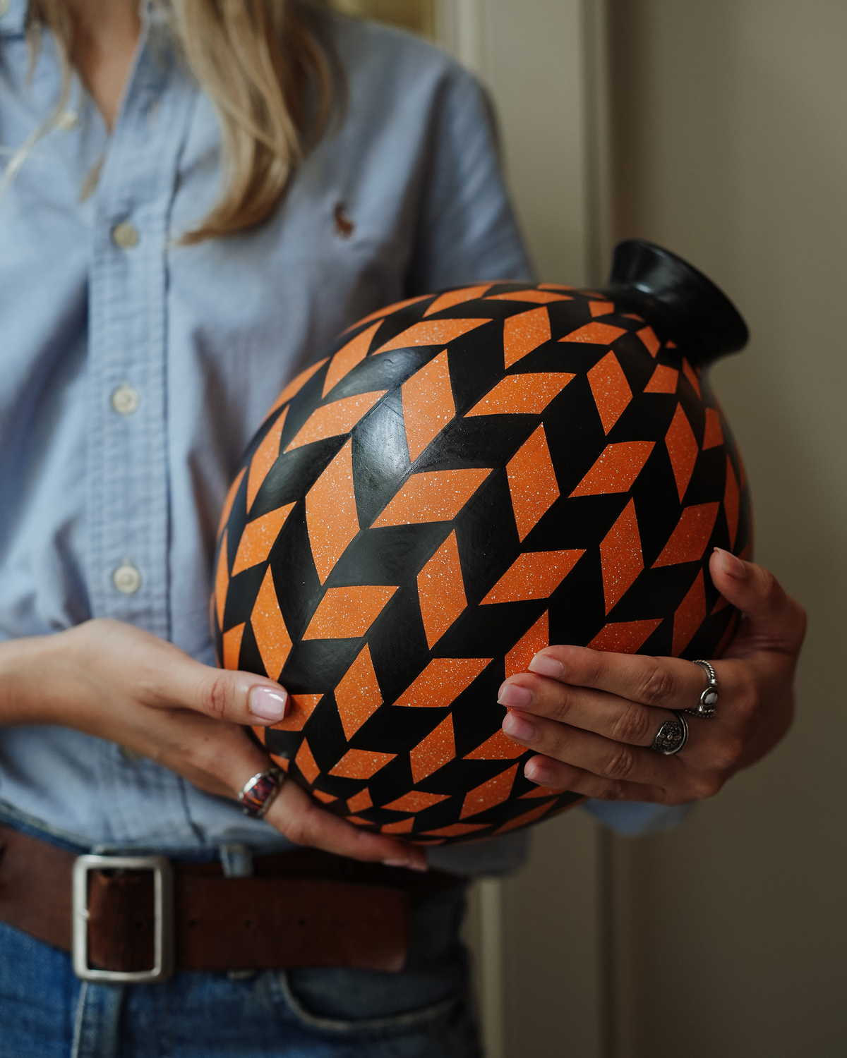 Hibiscus: handmade Nicaraguan ceramic round vessel with a bold orange and black chevron pattern, held in both hands