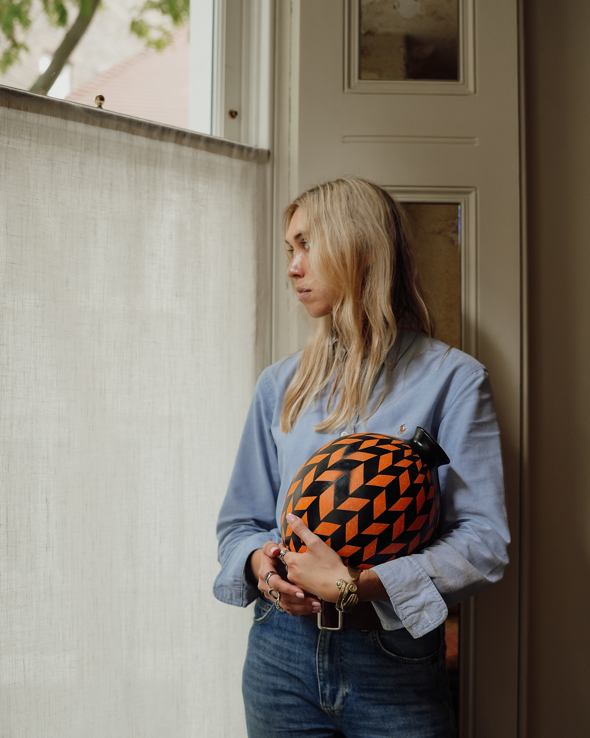 Hibiscus: handmade Nicaraguan ceramic round vessel with a bold orange and black chevron pattern, held by a woman standing by a window