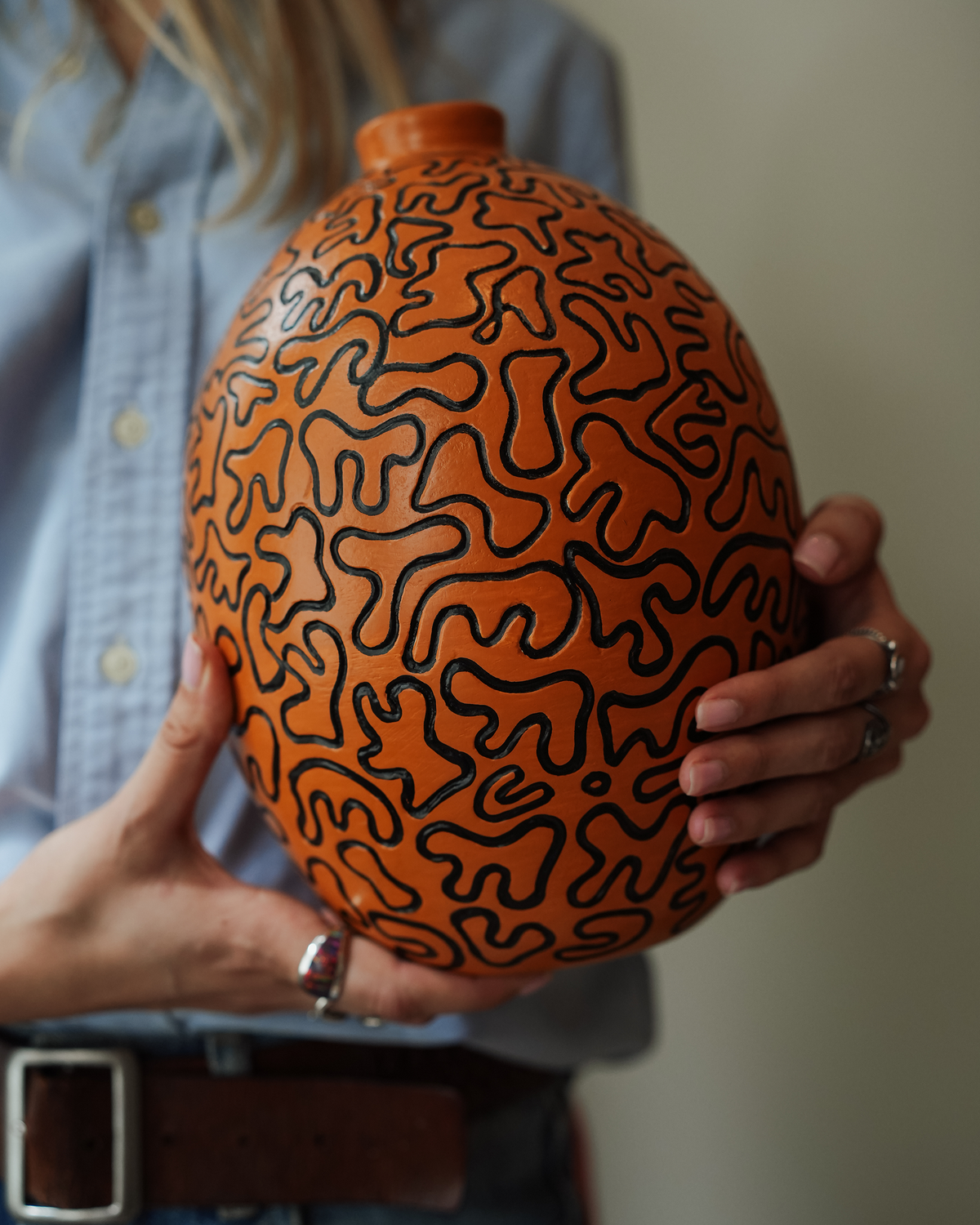 Hortensia: handmade Nicaraguan ceramic oval orange vessel with a meandering black line pattern, held in both hands