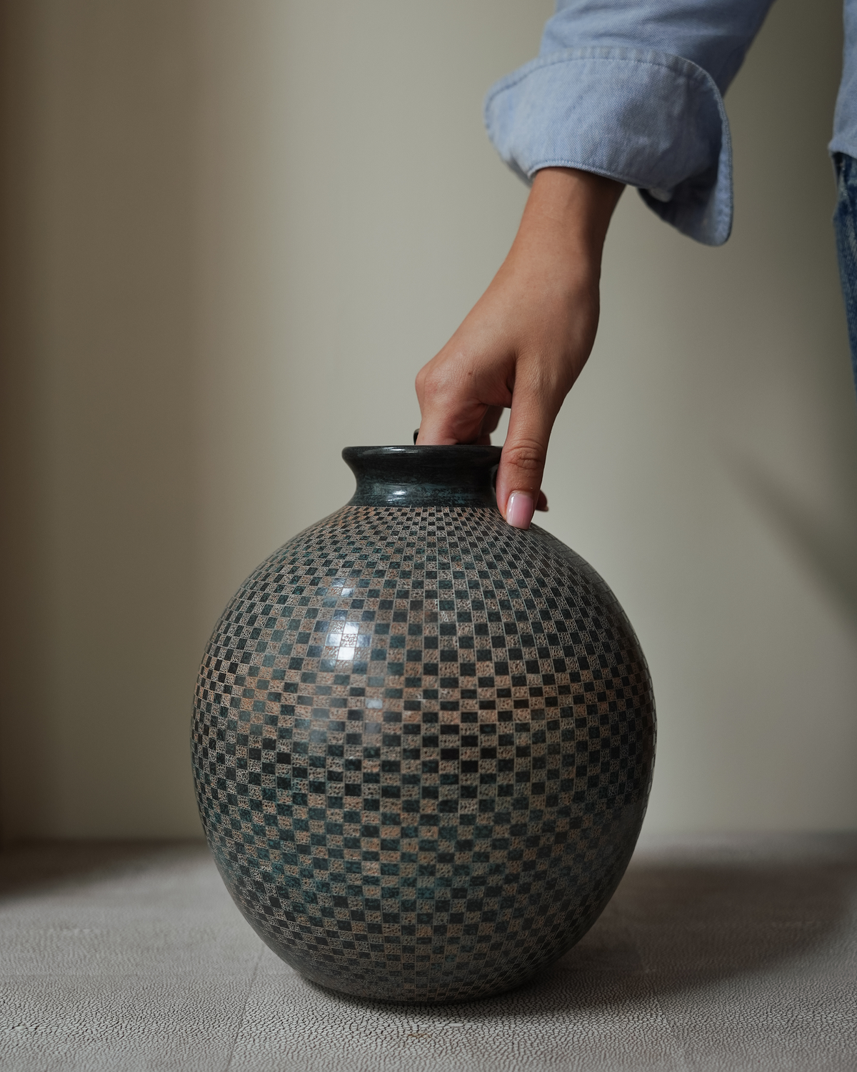 Lunaro: handmade Nicaraguan ceramic round grey-green vessel with a fine carved chequered pattern, with a hand on the rim