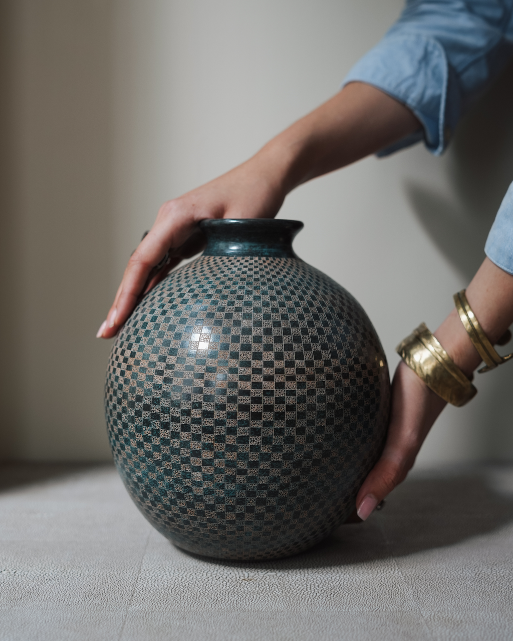 Lunaro: handmade Nicaraguan ceramic round grey-green vessel with a fine carved chequered pattern, steadied with both hands