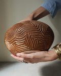 Serrano: handmade Nicaraguan ceramic round terracotta vessel deeply carved with wavy lines, cradled in two hands
