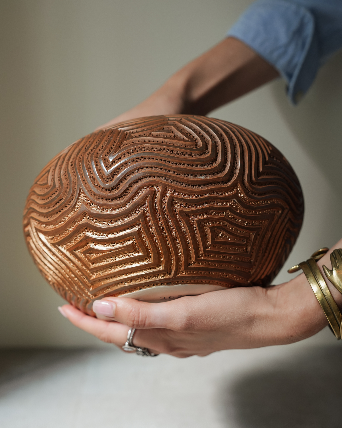 Serrano: handmade Nicaraguan ceramic round terracotta vessel deeply carved with wavy lines, cradled in two hands