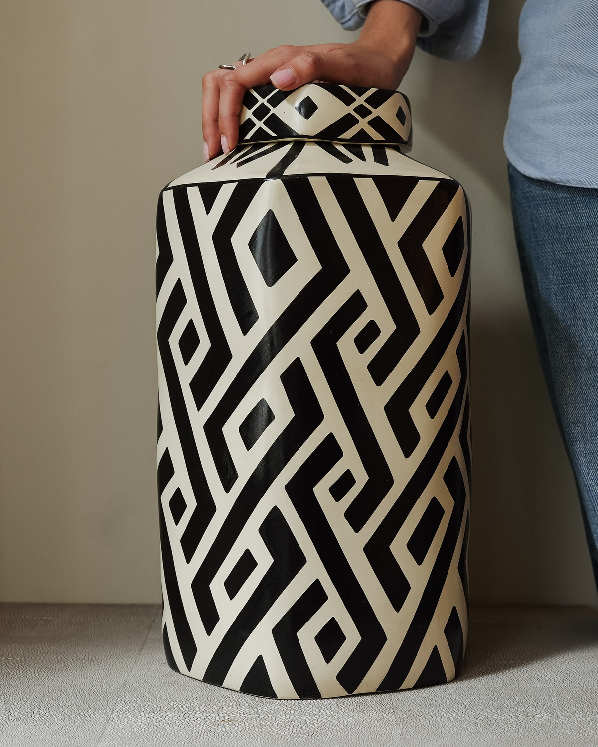 Zaruma: handmade Nicaraguan ceramic tall lidded jar with a bold black and white geometric pattern, with a hand resting on the lid
